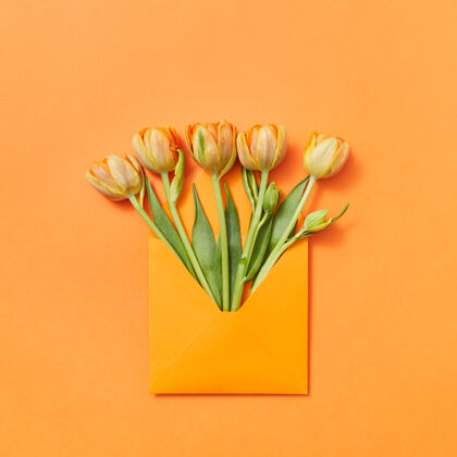 花束情书黄色的新采摘的鲜花放在一个手工信封里 橙色的背景上 蕾丝装饰文本.平面躺下花郁金香空