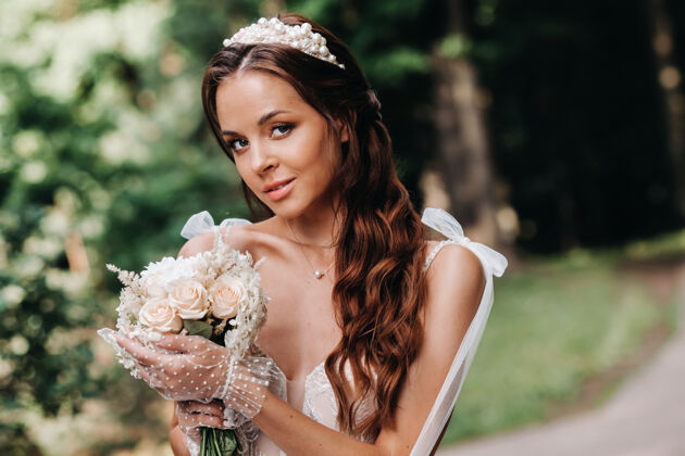 花一个优雅的新娘在一个自然公园里穿着白色的裙子和一束花束的肖像公园爱浪漫