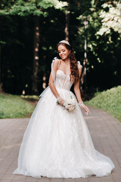 花艺一个优雅的新娘在一个自然公园里穿着白色的裙子和一束花束的肖像风景微笑婚纱