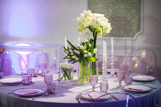 室内用百合花和郁金香装饰的节日晚餐 放在酒店内部的结婚桌上餐厅装修紫色调的庆祝桌玻璃晚上宴会