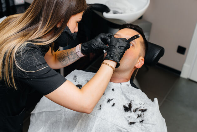 胡子一个专业的发型师在一个现代时尚的理发店剃须和削减一个年轻人的头发泡沫发型师男性