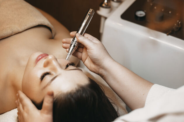 女性特写镜头：一位可爱的女性在健康中心接受美容师的面部射频治疗提升面部皮肤护理