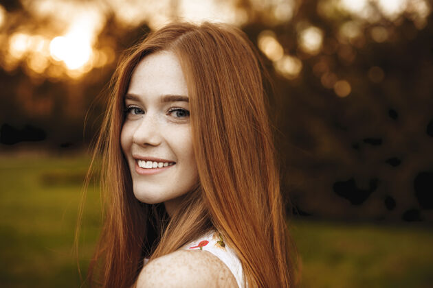 皮肤一个满脸雀斑的红发女孩在镜头前的特写照片 在外面夕阳的映衬下 她在肩上笑着女性户外特写