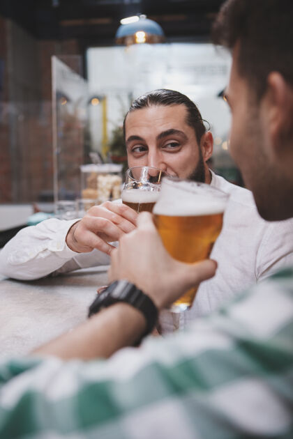 工艺垂直剪裁的男性朋友啜饮啤酒 在啤酒酒吧交谈的镜头啤酒酒吧酒精