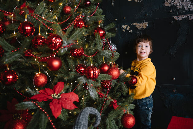 十二月一个快乐可爱的小男孩站在圣诞树旁 手里拿着一份礼物盒子孩子圣诞节心情.假期.圣诞节新年快乐微笑拇指圣诞老人