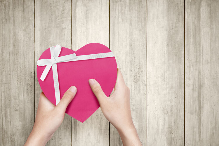 购买人手拿着一个粉色的礼品盒 上面有白色的丝带和心形的木纹墙情人节礼物天哪电子商务折扣消费主义
