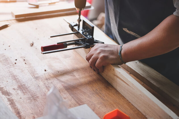 职业木工操作工正在用钻头在木头上钻孔 为客户组装和建造木制桌子看修理工匠