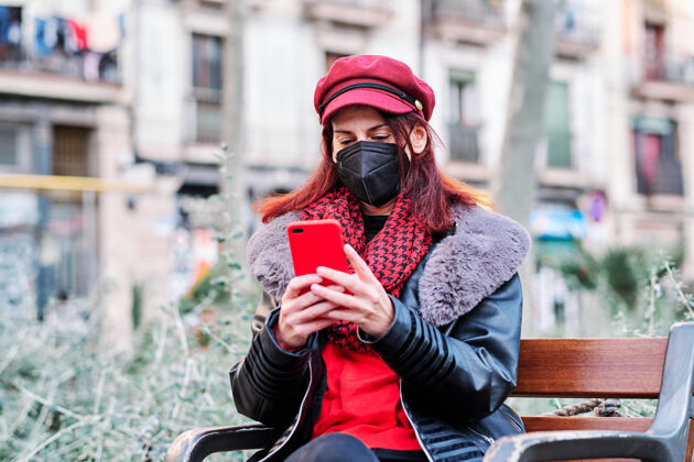 互联网一个戴着口罩坐在户外用手机发信息的女人公园新的正常寿命城市概念概念聊天应用程序社交距离
