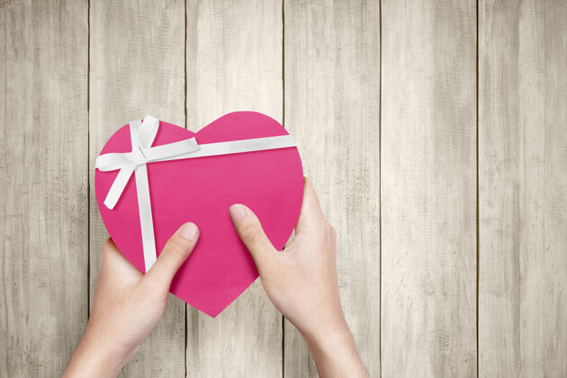 购买人手拿着一个粉色的礼品盒 上面有白色的丝带和心形的木纹墙情人节礼物天哪电子商务折扣消费主义