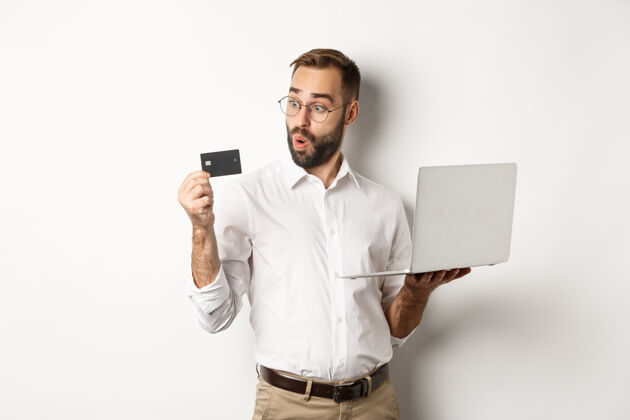 肖像在线购物惊奇商人拿着笔记本电脑 看着信用卡 站在白色的背景上ModelBusinessMan男