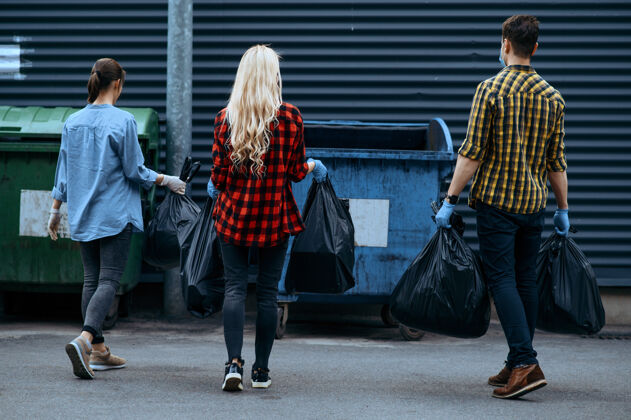 垃圾志愿者们把塑料垃圾袋放到户外的垃圾桶里 志愿者人清洁城市街道 生态修复 垃圾回收 生态关怀 环境清洁清洁垃圾青少年