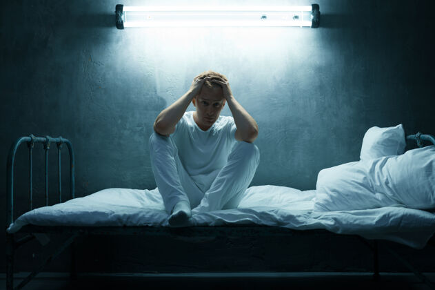 不快乐坐在床上的神经病男人 黑黑的房间每晚都有问题的人 抑郁和压力 悲伤 精神病院光幽灵问题