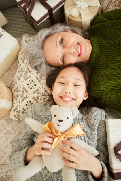 女人高角度观看快乐的孙女和奶奶一起躺在地板上微笑泰迪熊父母童年