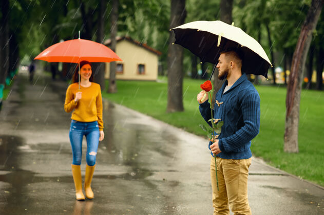 季节带着雨伞的情侣 在雨中的夏日公园浪漫约会戴曼带着红玫瑰在小路上等着他的女人 小巷里天气潮湿夫妇在一起天气