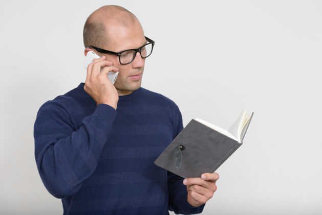 交谈年轻秃头书呆子一边看书一边打电话的画像男性使用书籍