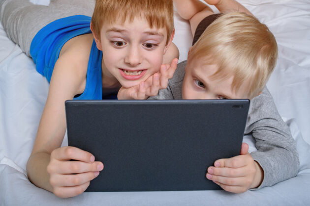 平板电脑两个男孩躺在床上看电视平板电脑.休闲小工具娱乐视觉视频