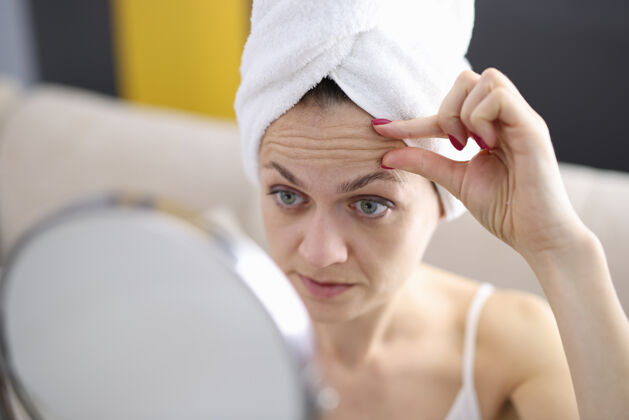 眉毛那个女人仔细检查她的额头上的皱纹镜子怎么了防止深层皱纹的概念预防健康治疗