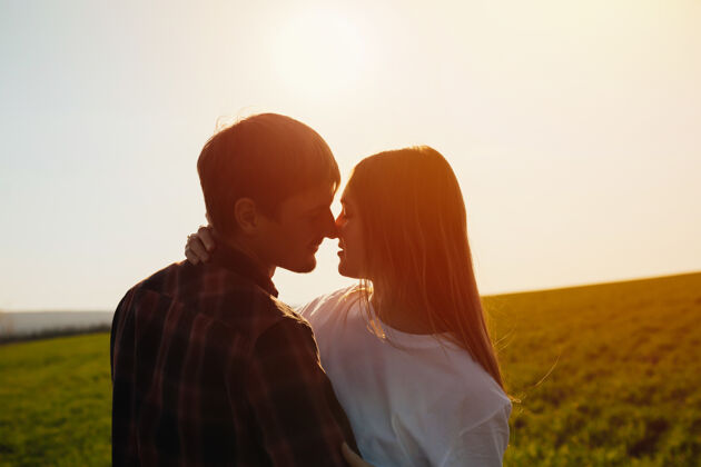 天空一对相爱的情侣在柔和温暖的橙色日出光中拥抱在美丽的绿色田野里年轻绿草女人