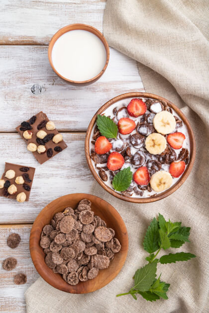 碗巧克力玉米片加牛奶和草莓放在白色木质表面和亚麻织物的木碗里草莓配料料理