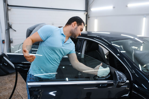 枪男工人清洗汽车进行着色 调校维修机械师在车库的车窗上涂乙烯基色 有色汽车玻璃工艺服务特写