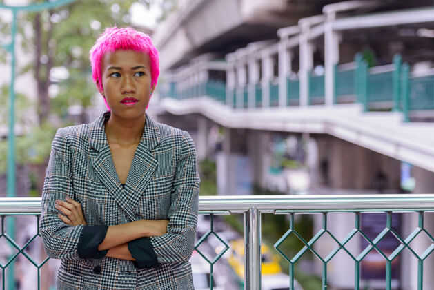 东南年轻叛逆的亚洲女商人的肖像 粉红色的头发在城市户外的人行天桥上客场行政头发