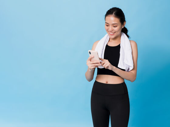 女孩亚洲美丽快乐的女人运动后用智能手机隔离在蓝色上年轻运动员女人