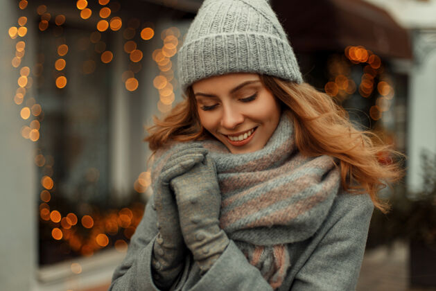 快乐假日黄灯附近的街道上 穿着时髦的灰色外套 戴着针织时髦的帽子 戴着围巾 带着神奇微笑的迷人美丽幸福女人时尚脸羊毛