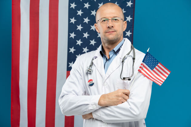 美国自信的中年医生戴着眼镜 穿着白大褂 举着美国国旗 站在星条旗下欢呼医护人员职业