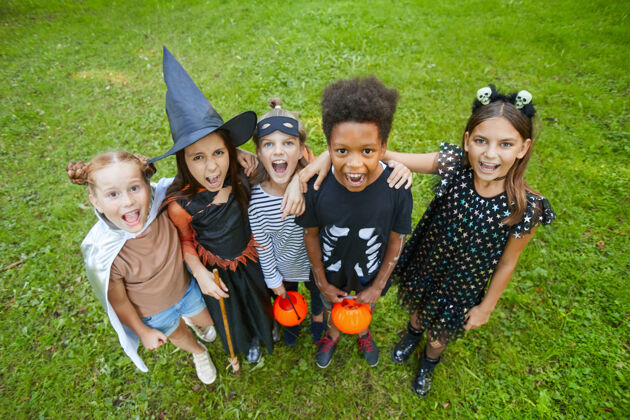 欢笑一群穿着万圣节服装的孩子站在户外绿草上对着镜头大喊大叫庆祝玩耍友谊