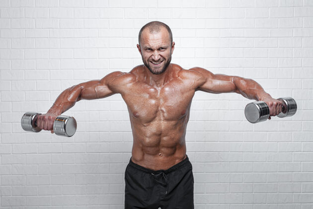 胸部健美运动员靠着砖墙用哑铃锻炼三角肌肖像健身砖墙