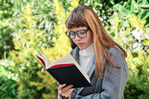 阅读一个蓝眼睛的白人金发女郎戴着眼镜在公园看书书女孩肖像
