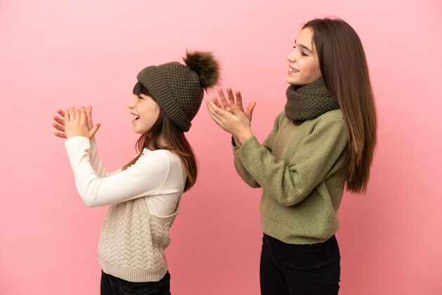 满意穿着冬装的小姐妹们在粉色背景上孤零零地鼓掌后在一个会议上发言天气小寒冷