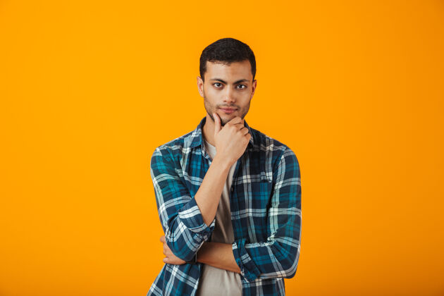 肖像一个穿着格子衬衫的沉思的年轻人孤零零地站在橙色的墙上期待思考男人