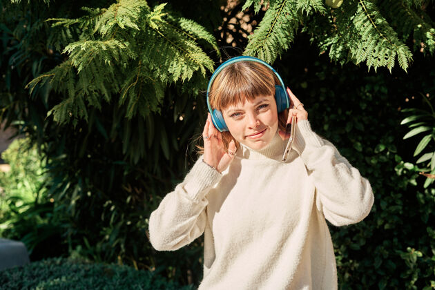肖像一个漂亮的白人女孩在公园里戴着蓝色耳机听音乐年轻女人金发