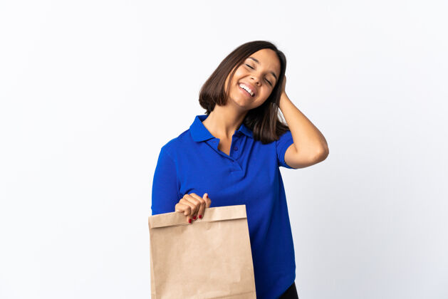 正面年轻的拉丁女子拿着一个杂货店的购物袋孤立地对白色微笑了很多自豪市场有趣