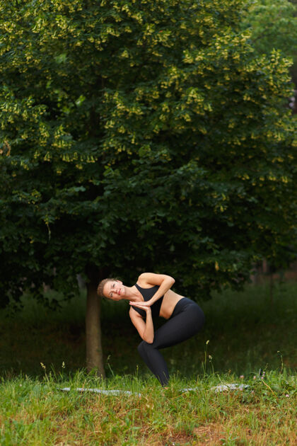 锻炼一个穿着黑色运动服的年轻女子在公园里做瑜伽的全长肖像 树上背景.垂直查看女人瑜伽健康