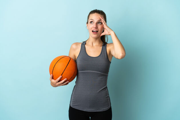 运动打篮球的年轻女子孤零零地站在蓝色的一边做着惊喜的手势 一边看一边稍后运动女人