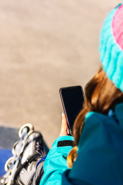 黑屏一个无法辨认的女滑冰者在城市滑冰场使用手机的后视图城市溜冰场滑冰概念和技术表演女性交通