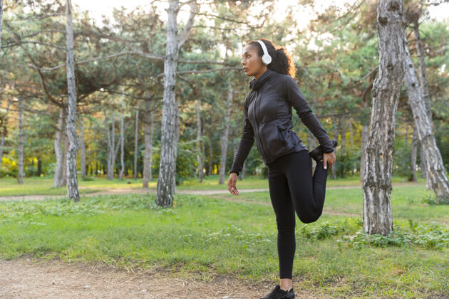锻炼20多岁的年轻女子穿着黑色运动服 在绿色公园里伸展身体伸展非洲无线