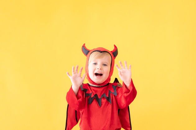 南瓜滑稽的孩子穿着魔鬼服装对着黄色的表面家庭恐怖传统