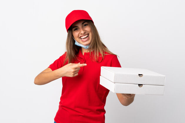 壁板披萨送货员拿着披萨 用口罩遮住隔离的白墙 指着它 保护自己免受冠状病毒的侵害防护展示信心