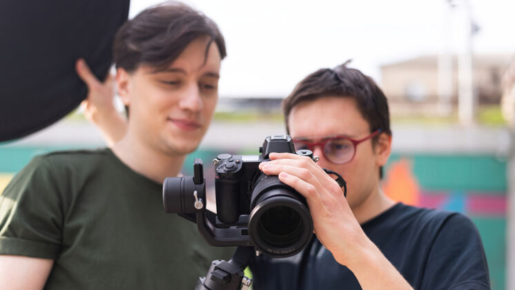 摄影两个年轻的微笑的摄影师在三脚架上看着相机拍照焦点背部男人