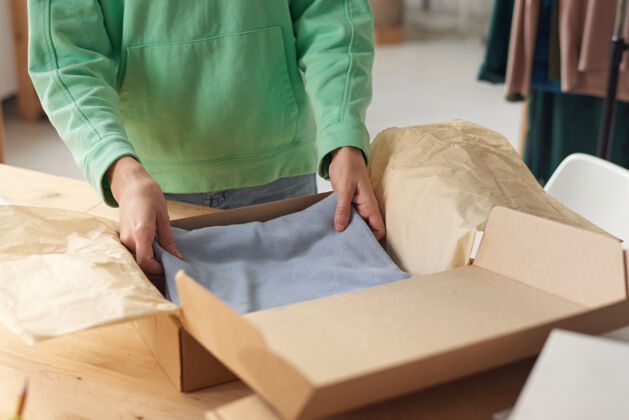 成人特写镜头：一个女人正在往盒子里装新衣服 她正在做一个包裹准备送货人手室内职业