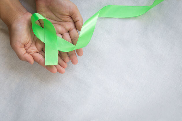 举行手拿翡翠绿或玉绿色丝带在白色织物墙上 有复制空间 象征肝癌意识 世界癌症日疾病肝脏癌症日