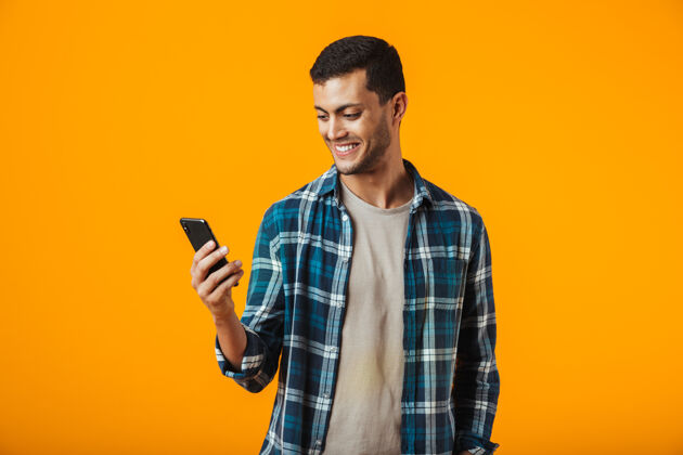 年轻一个穿着格子衬衫的年轻人孤零零地站在橘色的墙上 用着手机通信英俊站