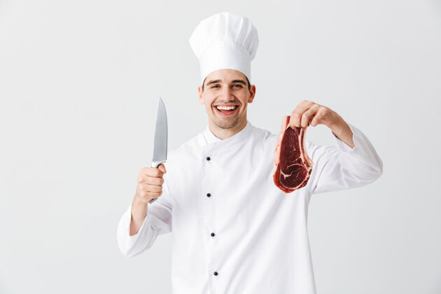 牛肉开朗的厨师穿着制服展示生牛排拿着刀隔着白墙新鲜手男人