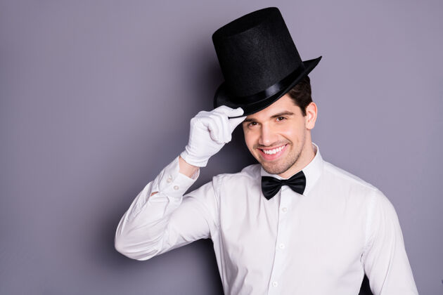 艺术家正面快活魔术师的特写照片男人准备娱乐观众触摸手黑色帽子隔离灰色墙壁看好时尚