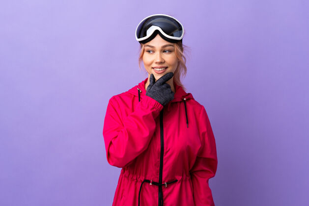 假期带着滑雪眼镜的滑雪者女孩孤零零地看着紫色的侧面 微笑着滑雪板运动滑雪