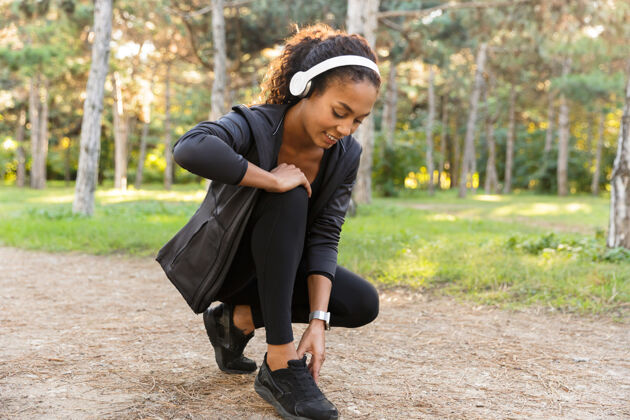 运动20多岁的女运动员穿着黑色运动服系鞋带 在绿色公园里奔跑女性女孩鞋带