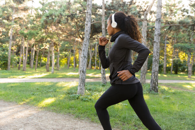 减肥20多岁的女强人穿着黑色运动服 戴着耳机 在绿色公园里跑步美国女孩吸引力